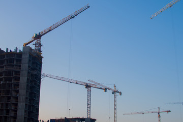 Silhouettes of tower cranes constructing a new residential building at a construction site against sunset background. Renovation program, development, concept of the buildings industry.