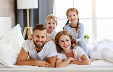 Obraz premium happy family mother, father and children laughing, playing and smiling in bed at home.