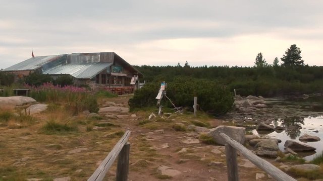 Leading from a small bridge to a mountain hut. After sunset in a surrounding of a lake, pine trees and rocks.Dolly along the bridge and turn towards the hut.
