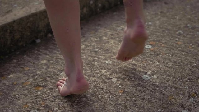 Close-up of a Caucasian female ballet dancer feet dancing in slow motion with a spin on a cloudy summers day on old concrete stairs barefoot with white henna tattoos on her feet.