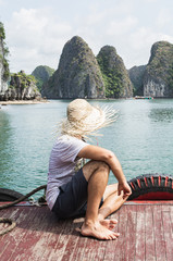 Young man in a straw hat enjoying the boat ride at Lan Ha Bay part of Halong bay, Cat Ba island, Vietnam