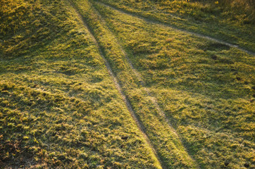 Two roads on a field in the countryside among green grass lit by the sun.