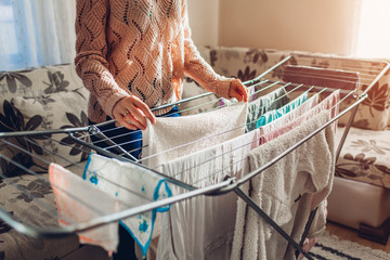 Woman hanging clean clothes on dryer after washing at home. Housekeeping and household chores