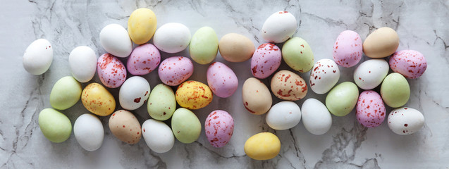 Happy Easter concept. Preparation for holiday. Easter pastel candy chocolate eggs sweets on trendy gray marble background. Simple minimalism flat lay top view copy space banner