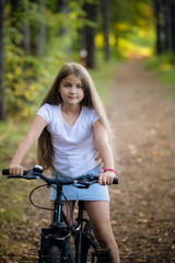 Obraz premium Little girl having fun on bike in the forest in autumn season