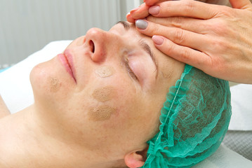 Beautician applies a natural moisturizing mask to the face of a young beautiful woman. Anti-aging...
