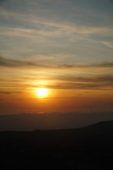 Breathtaking sunset over the sea with light reflection with a mountain range in front, dark clouds in the sky. Vertical image.
