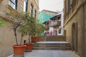 Fototapeta na wymiar Narrow empty ascending street with young trees in flower pots on the pavement and vintage balcones on historical buildings in Old Town Baku,Azerbaijan