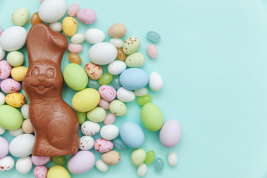 Happy Easter concept. Preparation for holiday. Easter candy chocolate eggs bunny and jellybean sweets isolated on trendy pastel blue background. Simple minimalism flat lay top view copy space.