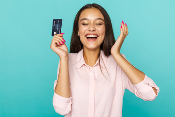 Fototapeta premium Happy and exited young lady with credit card standing isolated in the blue studio