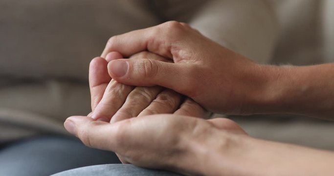 Young woman holding stroking senior grandparent female hand, closeup