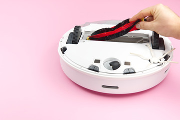 white robot vacuum cleaner on a pink background. The procedure for cleaning the robot vacuum cleaner after cleaning. future home technology.