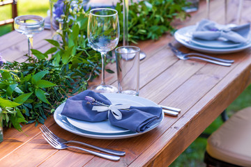 Beautifully decorated wooden table in a summer open-air cafe. Green branch and fresh flowers table decoration
