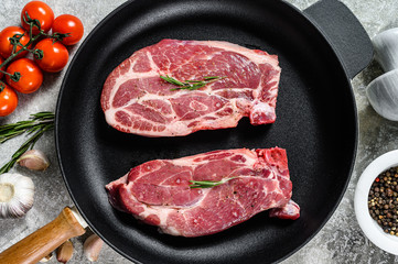 Raw pork steak in a frying pan. Marbled farm meat. Gray background. Top view