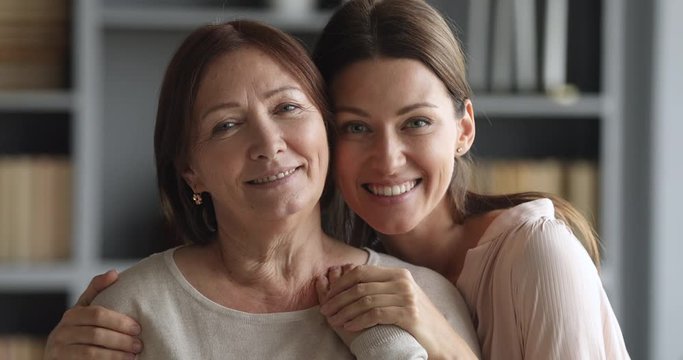 Beautiful adult daughter hugging older mature mum looking at camera