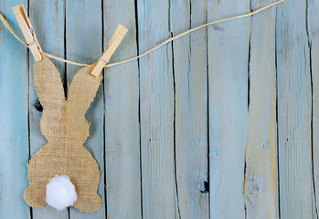Bunny shape in burlap with a cotton swab tail hanging from twine by clothespins. Background is blue...