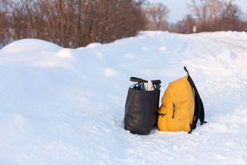A yellow camping backpack filled with things is standing on the snow on the side of the road. Hitchhiking concept in winter