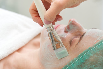 Beautician applies a natural moisturizing mask to the face of a young beautiful woman. Anti-aging...