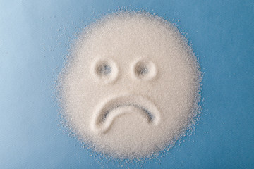 Salt scattered on black surface. Drawn sad face. Concept- diet, harm to health from excessive consumption of salt and sugar