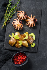 Roasted octopus. Baked potatoes and celery. Black background. Top view