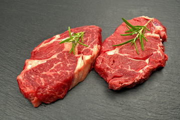 Raw rib eye steak with spices and vegetables. Ingredients for restaurant meal. Fresh meat, salt, rosemary, thyme, chilli, cherry tomatoes, garlic on black stone. Food background.
