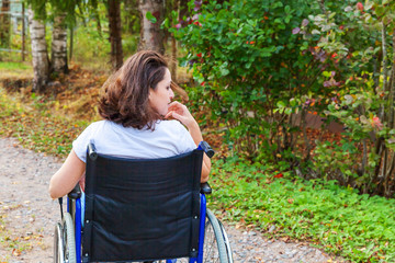 Young happy handicap woman in wheelchair on road in hospital park enjoying freedom. Paralyzed girl in invalid chair for disabled people outdoor in nature. Rehabilitation concept.