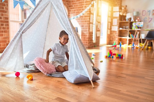 Beautiful african american toddler playing inside tipi smiling at kindergarten