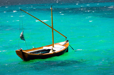 Fototapeta premium small and old fishing wooden boat with nobody on board sailing in the green Aegean sea. The wooden boa is waiting at harbor waiting for fisherman to sail. Waves, foam and tides hit the boat