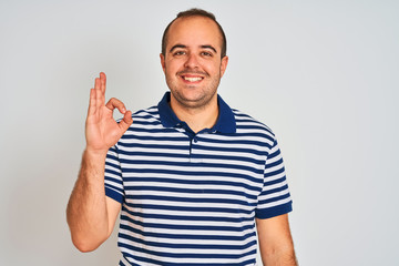 Naklejka premium Young man wearing casual striped polo standing over isolated white background smiling positive doing ok sign with hand and fingers. Successful expression.