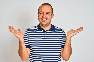 Naklejka premium Young man wearing casual striped polo standing over isolated white background smiling showing both hands open palms, presenting and advertising comparison and balance