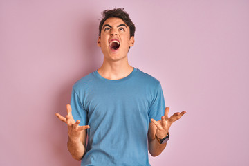 Teenager boy wearing casual t-shirt standing over blue isolated background crazy and mad shouting...