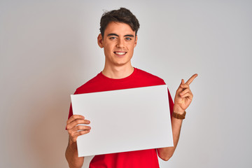 Teenager boy holding advertising banner with blank space over isolated background very happy...