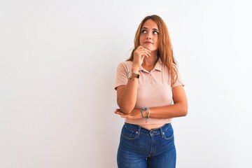 Young redhead woman stading over white isolated background with hand on chin thinking about question, pensive expression. Smiling with thoughtful face. Doubt concept.