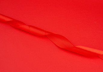 twisted red silk shiny ribbon on a red background, festive design element