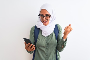 Young Arab student woman wearing hijab using smartphone over isolated background screaming proud and celebrating victory and success very excited, cheering emotion