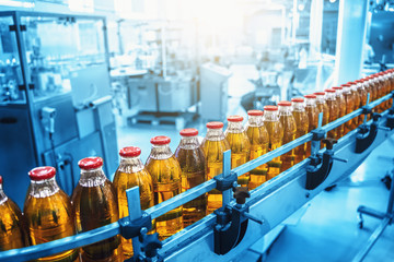 Industrial interior of natural juice plant production in blue color. Conveyor belt, filled bottles on beverage factory, industry production line, toned