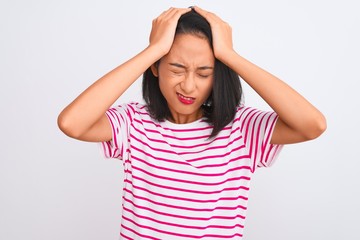 Young chinese woman wearing striped t-shirt standing over isolated white background suffering from headache desperate and stressed because pain and migraine. Hands on head.