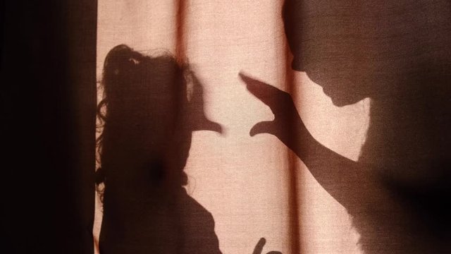Unrecognizable mother and child of primary school age telling stories using shadow  talking dog's heads when sitting behind the curtains at home on a sunny day and spend time together