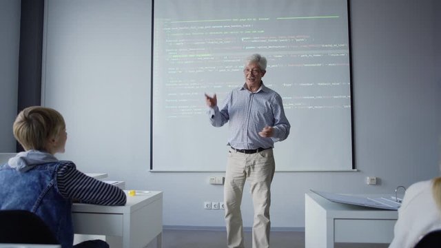 Follow shot of optimistic aged teacher spreading hands showing balance explaining computer science to children in school class