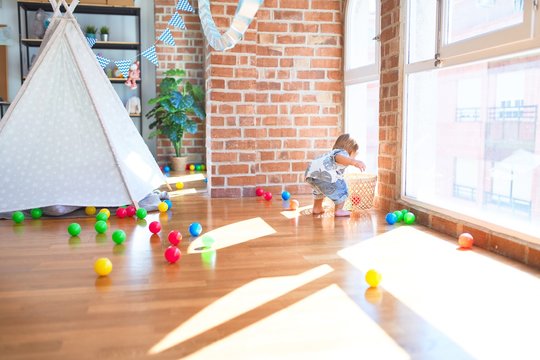 Adorable toddler playing with balls around lots of toys at kindergarten