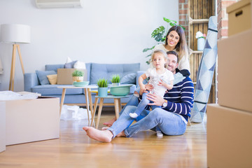 Beautiful family sitting on the floor playing with his kid at new home around cardboard boxes