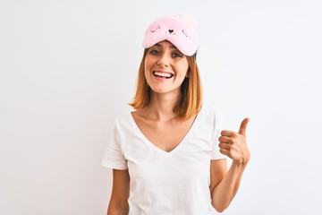 Beautiful redhead woman wearing sleeping mask over isolated background doing happy thumbs up...