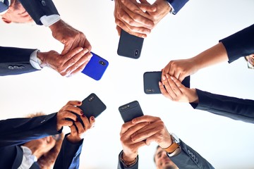 Group of business workers smiling happy and confident. Standing on a circle with smile on face using smartphone together at the office.