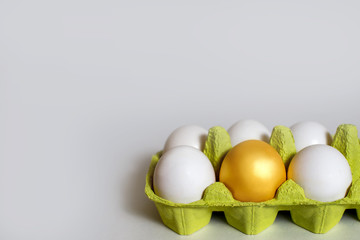 Chicken golden egg with white eggs in a box on white. Conceptual photo of team leadership. The best specimen surrounded by ordinary objects, Easter