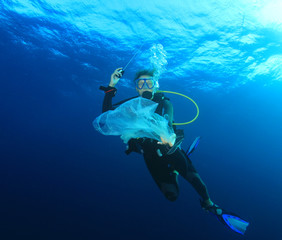 Young woman scuba diver picks up plastic trash from ocean. Beach cleanup concept 