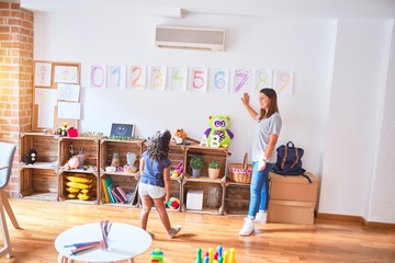 Beautiful teacher teaching maths to toddler girl playing at kindergarten