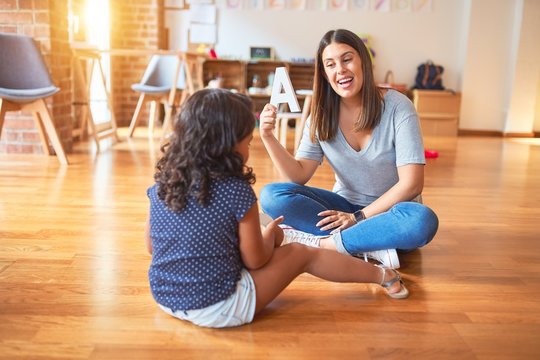 Beautiful teacher teaching alphabet to student toddler girl at kindergarten