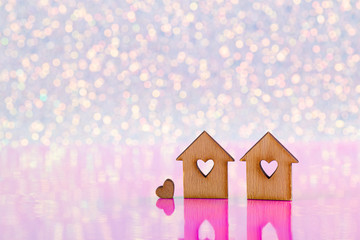 Obraz na płótnie Canvas Two wooden houses with hole in form of heart on glitter shiny light and pink background with bokeh lights.