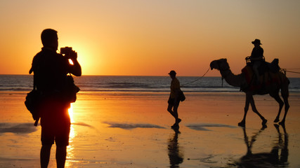 Silhouette of travel photographer photographing  tourist on camel ride convoy