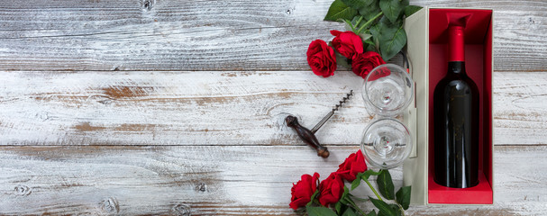 Happy Valentines Day celebration with red roses and a bottle of wine on white weathered wooden background with copy space